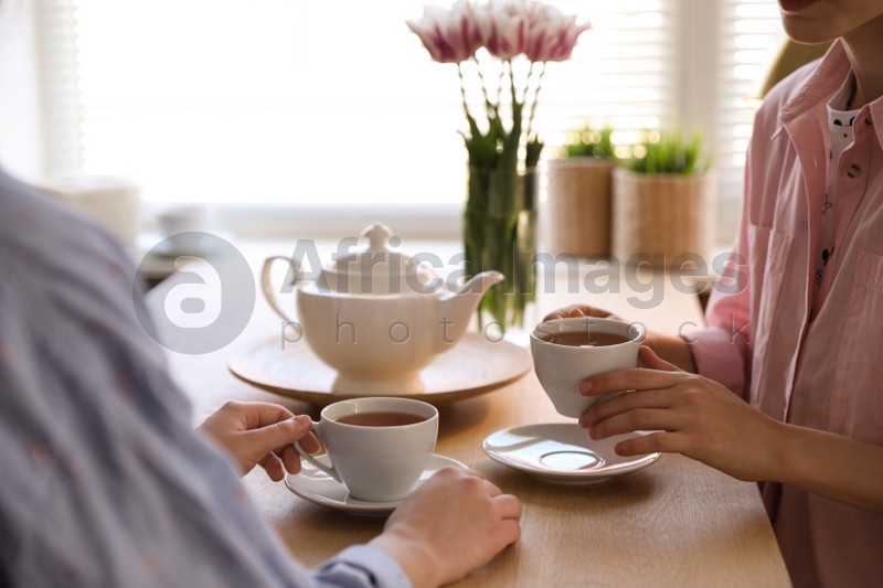 Women with cups of tea at table near window indoors, closeup