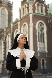 Young nun with hands clasped together while praying near cathedral outdoors