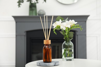 Reed diffuser and vase with bouquet on white table in room