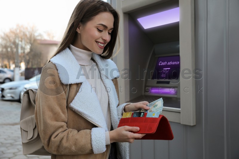 Woman putting money into wallet near cash machine outdoors