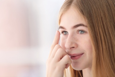 Teenage girl putting contact lens in her eye on blurred background