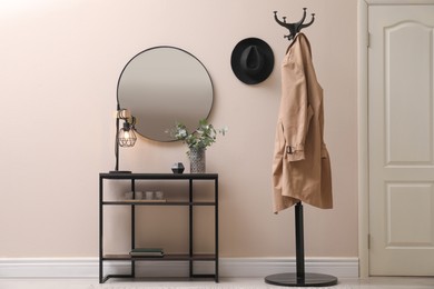Photo of Console table, clothes rack and mirror on beige wall in hallway. Interior design