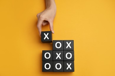 Woman playing tic tac toe game on yellow background, top view
