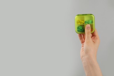 Woman holding plastic box with different pills on light grey background, closeup. Space for text