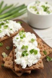 Photo of Crispy crackers with cottage cheese and green onion on wooden board, closeup