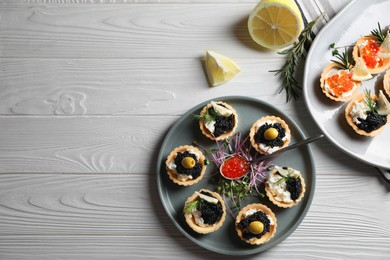 Photo of Delicious tartlets with red and black caviar served on white wooden table, flat lay. Space for text