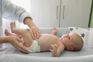 Photo of Mother changing baby's diaper on table indoors, closeup