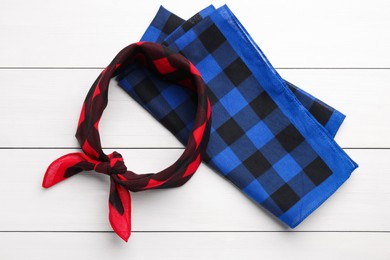 Tied and folded checkered bandanas on white wooden table, flat lay