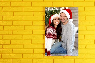 Canvas with printed photo happy couple wearing Santa hats on yellow brick wall, space for text