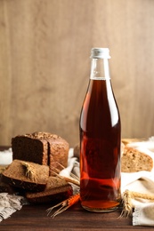 Photo of Bottle of delicious fresh kvass, spikelets and bread on wooden table