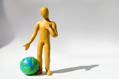 Yellow plasticine human figure with planet on white background, space for text