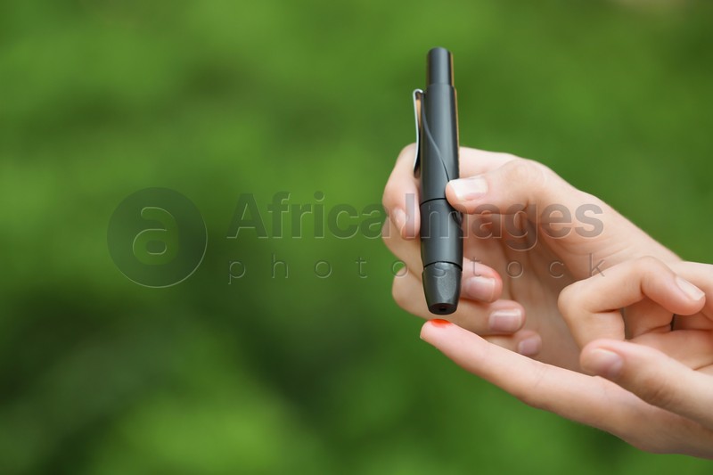 Woman using lancet pen on blurred background. Diabetes control