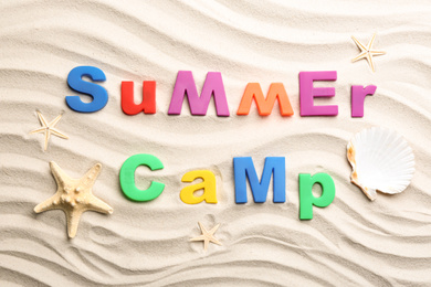 Photo of Flat lay composition with phrase SUMMER CAMP made of magnetic letters on sand
