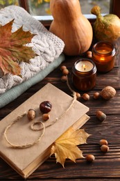 Photo of Book with autumn leaf as bookmark, acorns, scented candles and warm sweaters on wooden table