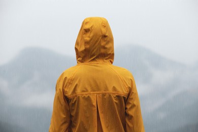 Woman in raincoat enjoying mountain landscape under rain, back view