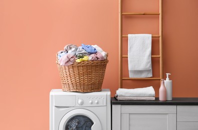 Wicker basket with dirty laundry on washing machine near coral wall indoors