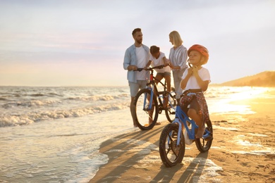 Happy family with bicycles on sandy beach near sea