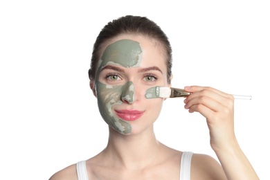Young woman applying clay mask on her face against white background. Skin care