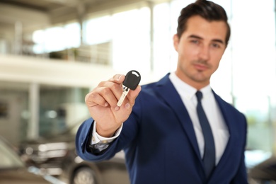 Young salesman with car key in modern dealership, focus on hand