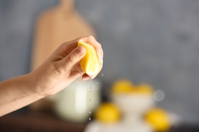 Young woman squeezing lemon on blurred background