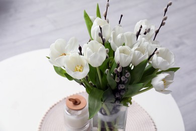 Beautiful bouquet of willow branches and tulips in vase on white table, above view