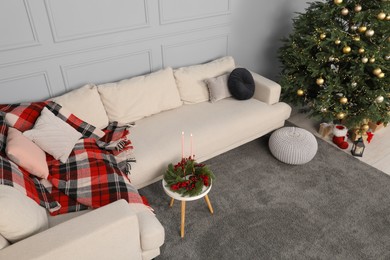 Photo of Beautiful Christmas tree, sofa and candles on table in living room