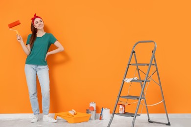 Photo of Happy designer with roller and painting equipment near freshly painted orange wall indoors