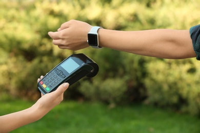 Woman using terminal for contactless payment with smart watch outdoors