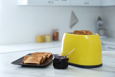 Modern toaster with slices of bread and jam on white marble table in kitchen