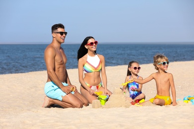 Photo of Happy family playing on sandy beach near sea. Summer holidays