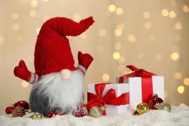 Cute Christmas gnome, gift boxes and festive decor on snow against blurred lights