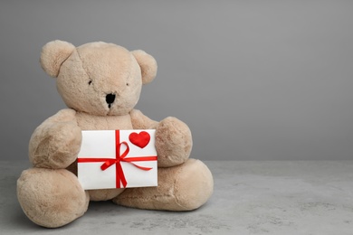 Cute teddy bear with envelope on light grey stone table, space for text. Valentine's day celebration