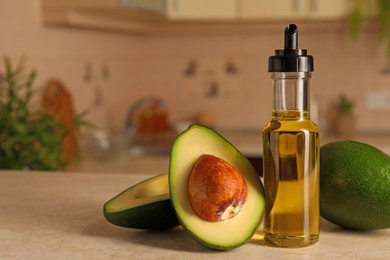Photo of Fresh avocados and cooking oil on beige marble table in kitchen, space for text