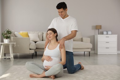 Husband massaging his pregnant wife in living room. Preparation for child birth