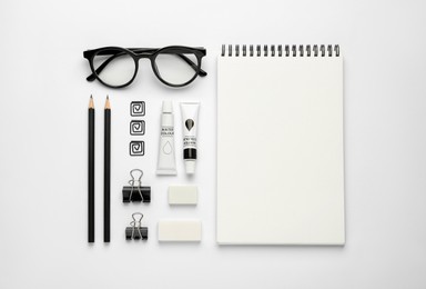 Composition with sketchbook, glasses and stationary on white background, top view