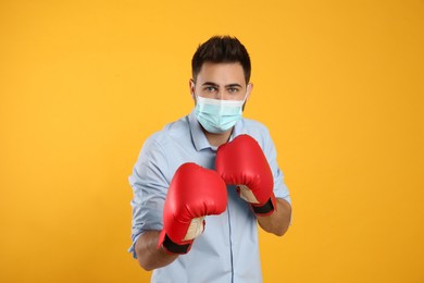 Man with protective mask and boxing gloves on yellow background. Strong immunity concept