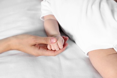 Mother holding hand of her little baby on bed, closeup