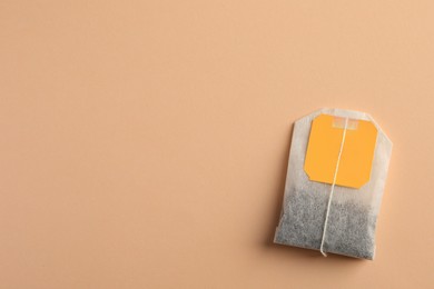 New tea bag with tab on pale orange background, top view. Space for text