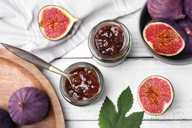 Photo of Glass jars of tasty sweet fig jam and fruits on white wooden table, flat lay