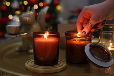 Photo of Woman lighting candle in room decorated for Christmas, closeup