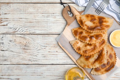 Delicious fried chebureki with sauce on white wooden table, flat lay. Space for text