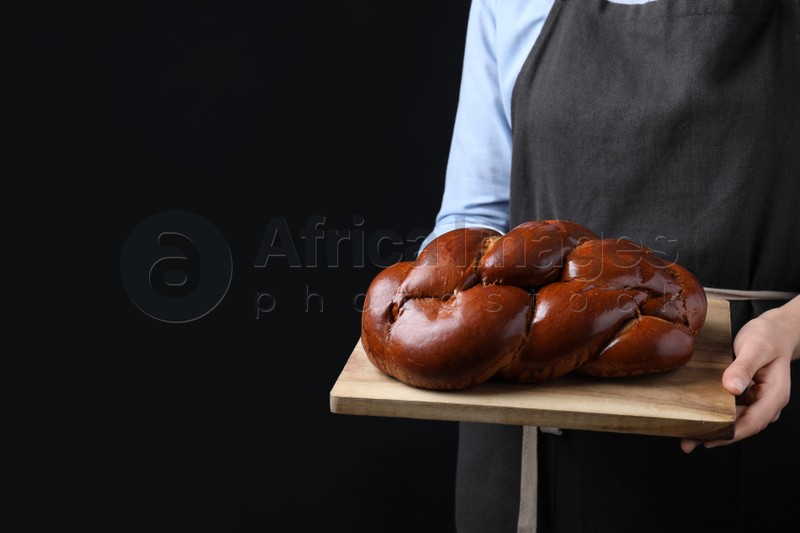 Photo of Closeup view of woman holding homemade braided bread on black background, space for text. Traditional Shabbat challah