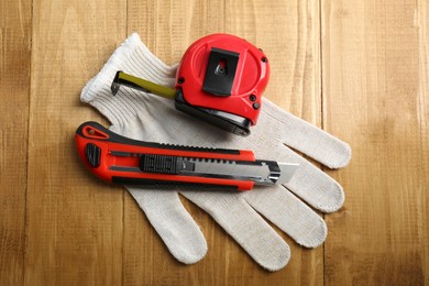 Photo of Utility knife, measuring tape and glove on wooden table, top view