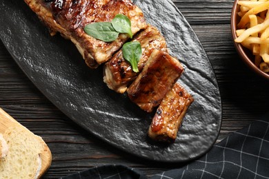 Photo of Delicious grilled ribs served on black wooden table, flat lay