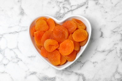 Heart shaped bowl with apricots on marble background, top view. Dried fruit as healthy food