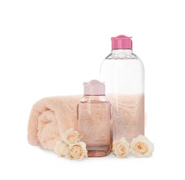 Bottles of micellar cleansing water, rolled towel and flowers on white background