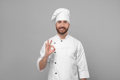 Photo of Smiling mature chef showing ok gesture on grey background