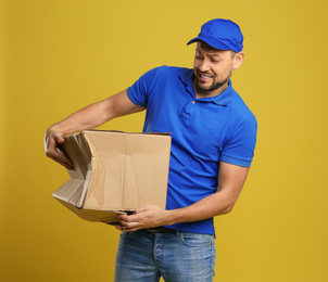 Emotional courier with damaged cardboard box on yellow background. Poor quality delivery service