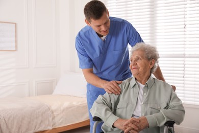 Caregiver assisting senior woman in wheelchair indoors. Home health care service