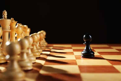 Black pawn in front of white pieces on wooden board against dark background. Competition concept